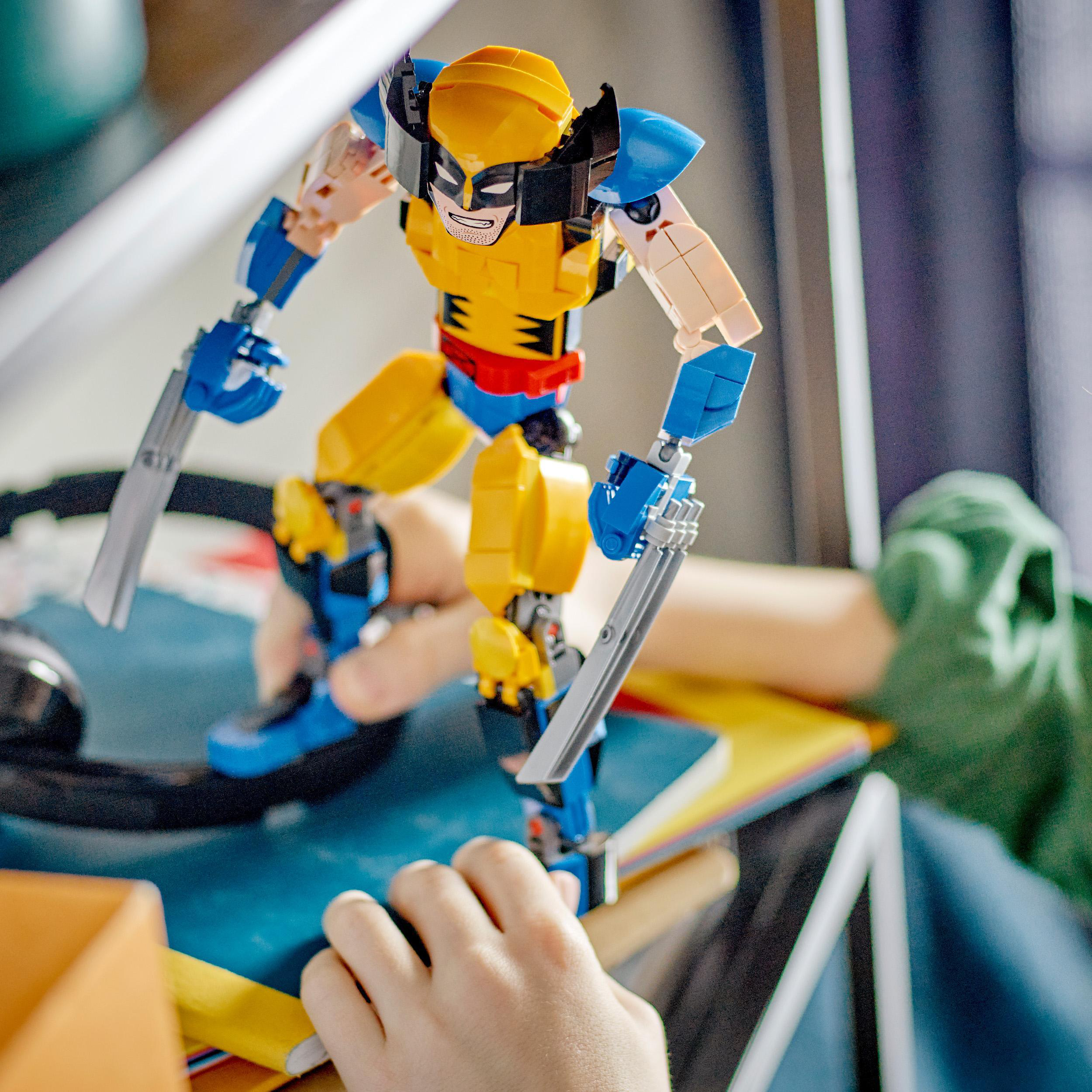 Lego Wolverine Figur. Gelb-blauer Anzug. Hände halten Krallen. Kinderhände sind sichtbar.