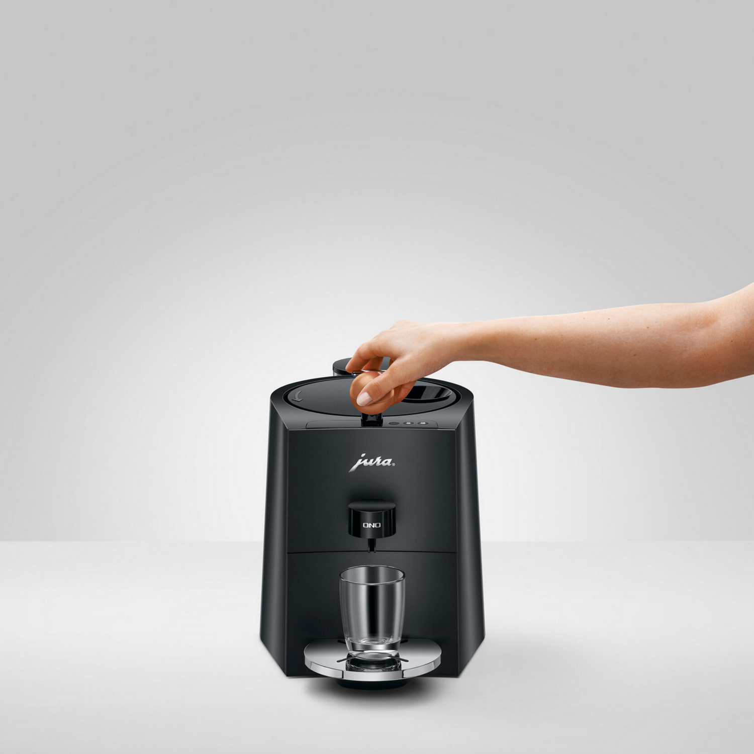 Hand placing a glass under a black Jura coffee machine. White background.