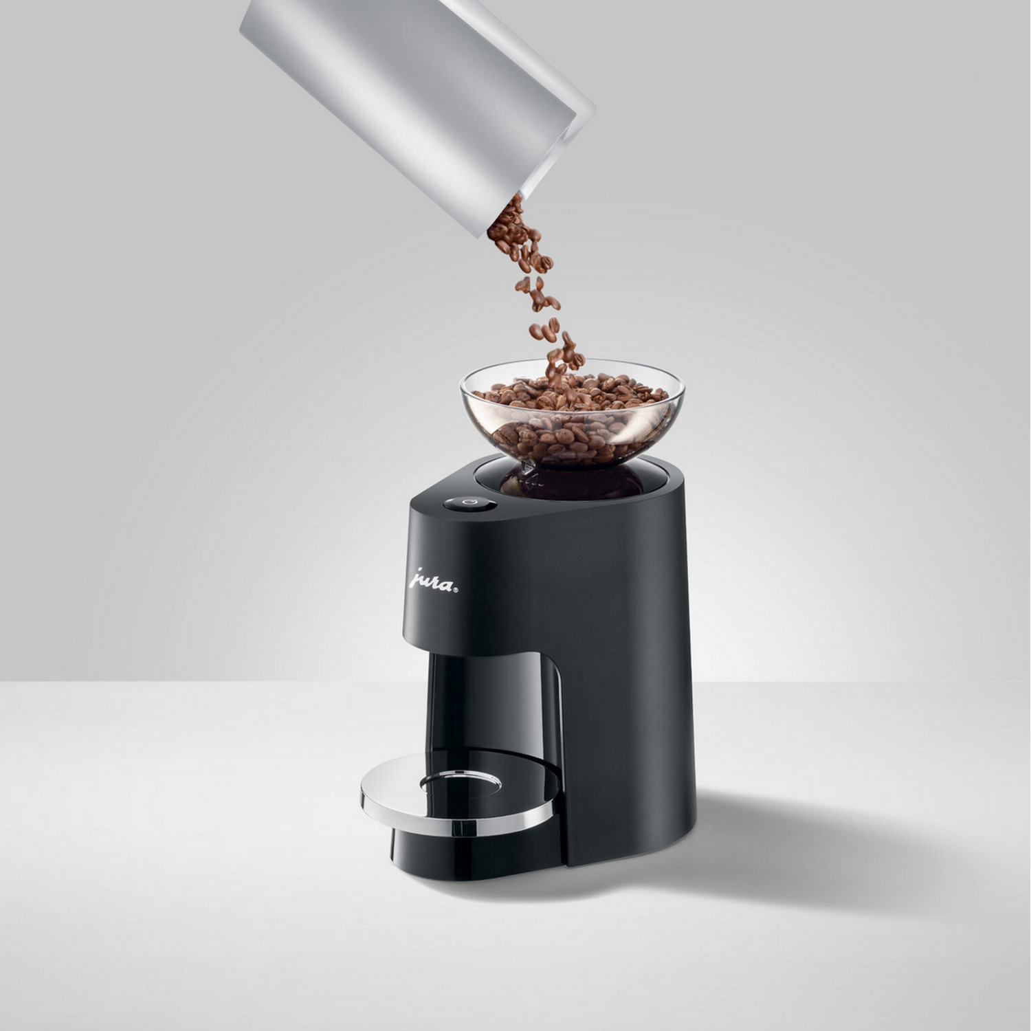 Coffee beans pouring into a glass bowl on a black coffee machine.