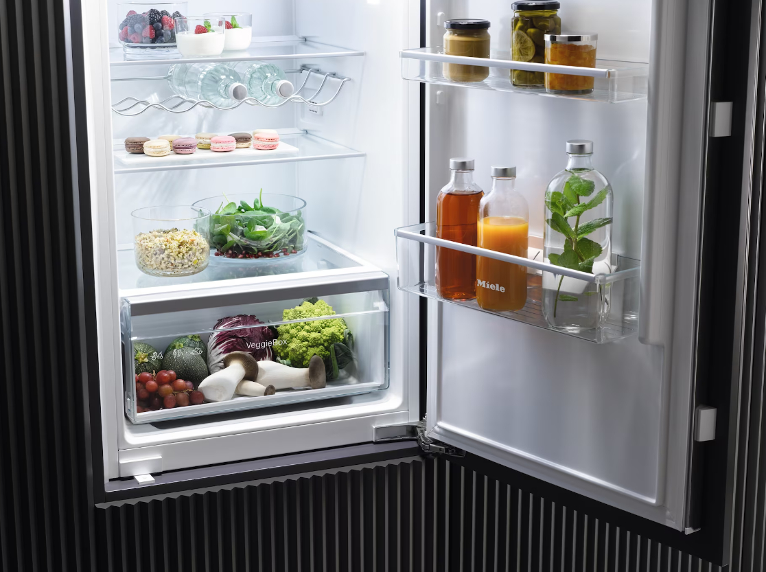 Offener Kühlschrank, der Regale mit Lebensmitteln zeigt. Enthält Gemüse, Obst und Getränke.