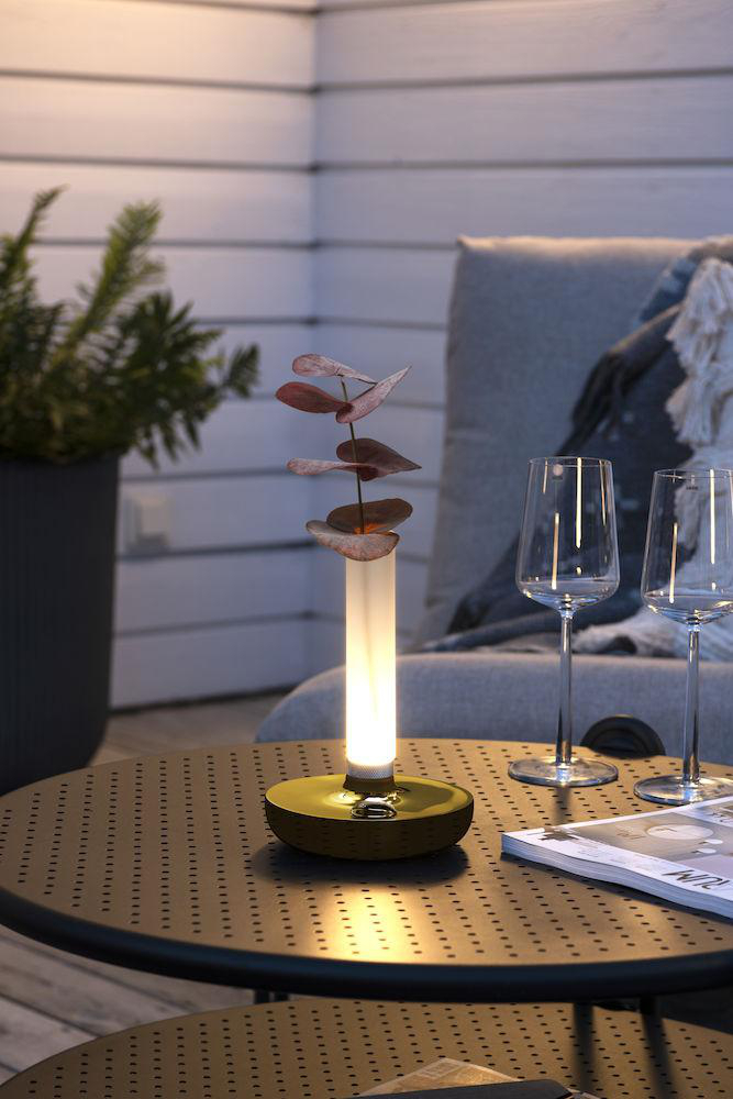 Eine beleuchtete Tischlampe mit Eukalyptuszweigen, Weingläsern und einer Zeitschrift.