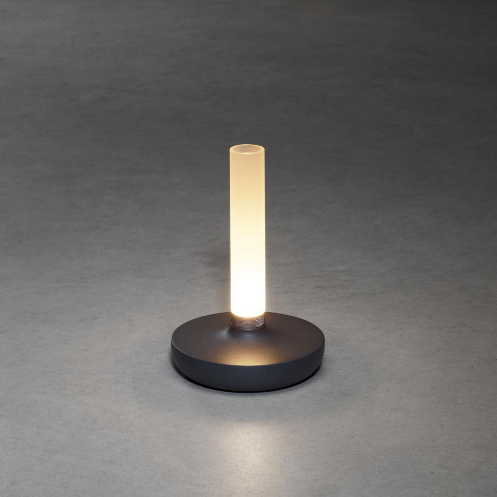 Eine zylindrische Lampe mit einem leuchtenden weißen Licht. Sie steht auf einem dunkelgrauen, kreisförmigen Sockel.