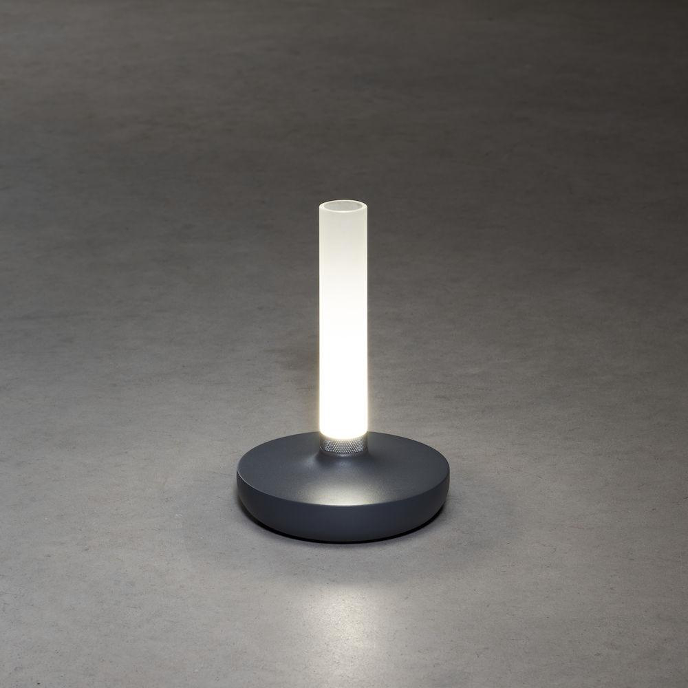 Graue Tischlampe mit zylindrischem Licht und kreisförmigem Fuß, beleuchtet.