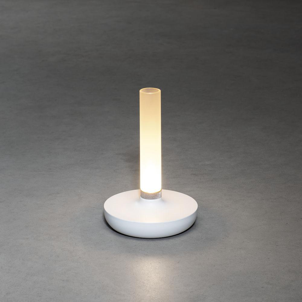 Weiße zylindrische Lampe mit leuchtendem Licht. Sie hat einen abgerundeten Sockel auf grauer Oberfläche.