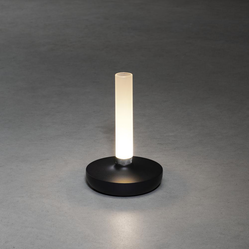 Moderne, zylindrische LED-Lampe. Schwarzer Sockel und ein leuchtendes weißes Rohr auf grauer Oberfläche.