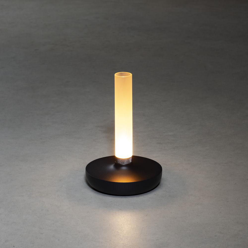 Eine schwarz-weiße Lampe mit zylindrischer Milchglasröhre und rundem schwarzen Sockel, von innen beleuchtet.