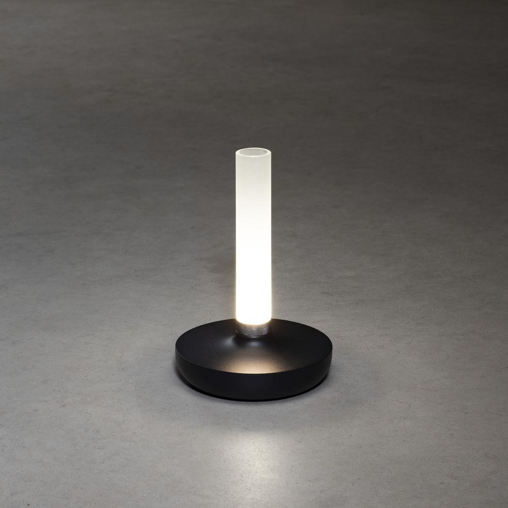Eine schwarze Lampe mit rundem Sockel und weißem Lichtrohr auf grauem Untergrund.