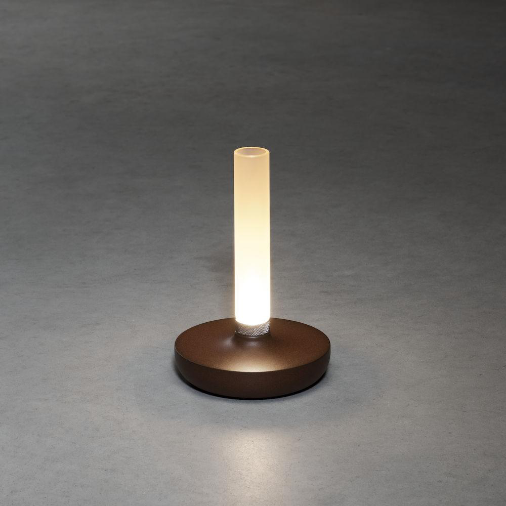 Eine braune Lampe mit einem leuchtenden weißen zylindrischen Licht auf einer grauen Oberfläche. Der Sockel ist rund.
