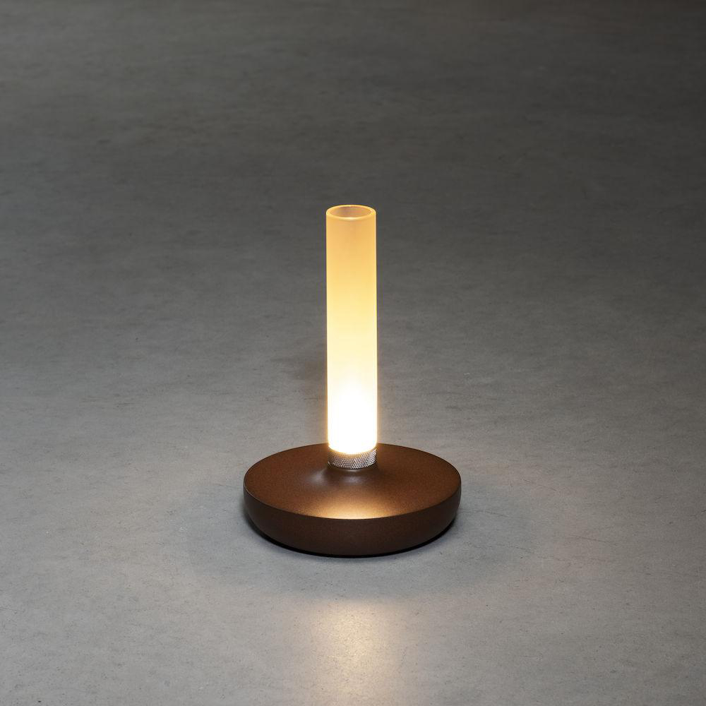 Ein brauner, kreisförmiger Sockel mit einer vertikalen, beleuchteten Röhrenlampe. Grauer Bodenhintergrund.