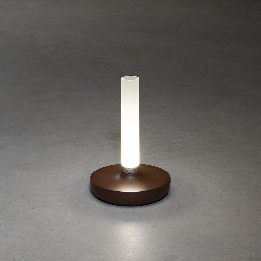 Eine braune Lampe mit weißem Licht steht auf grauem Untergrund.