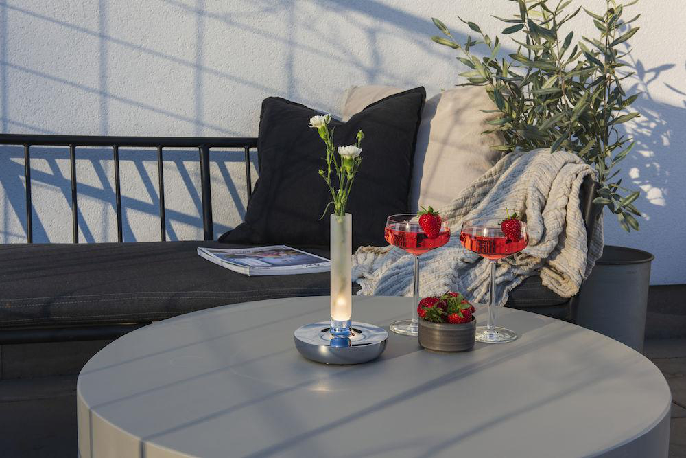 Tischdeko: Blumen in Vase, Getränke, Erdbeeren auf rundem Tisch.
