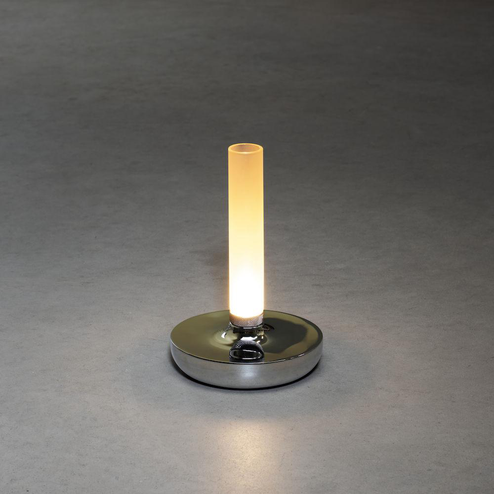 Eine zylindrische Lampe mit einer leuchtenden Röhre, auf einem glänzenden, runden, silbernen Sockel.
