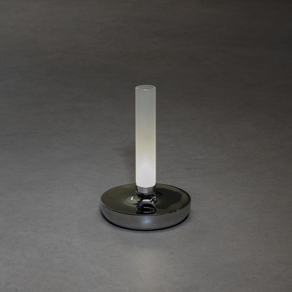 Eine hohe, zylindrische Lampe mit weißem Licht. Silberner Sockel auf grauer Oberfläche.