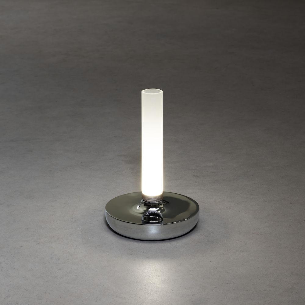 Eine moderne Tischleuchte mit silbernem Sockel und zylindrischem weißem Licht. Auf grauer Oberfläche platziert. Sie leuchtet.
