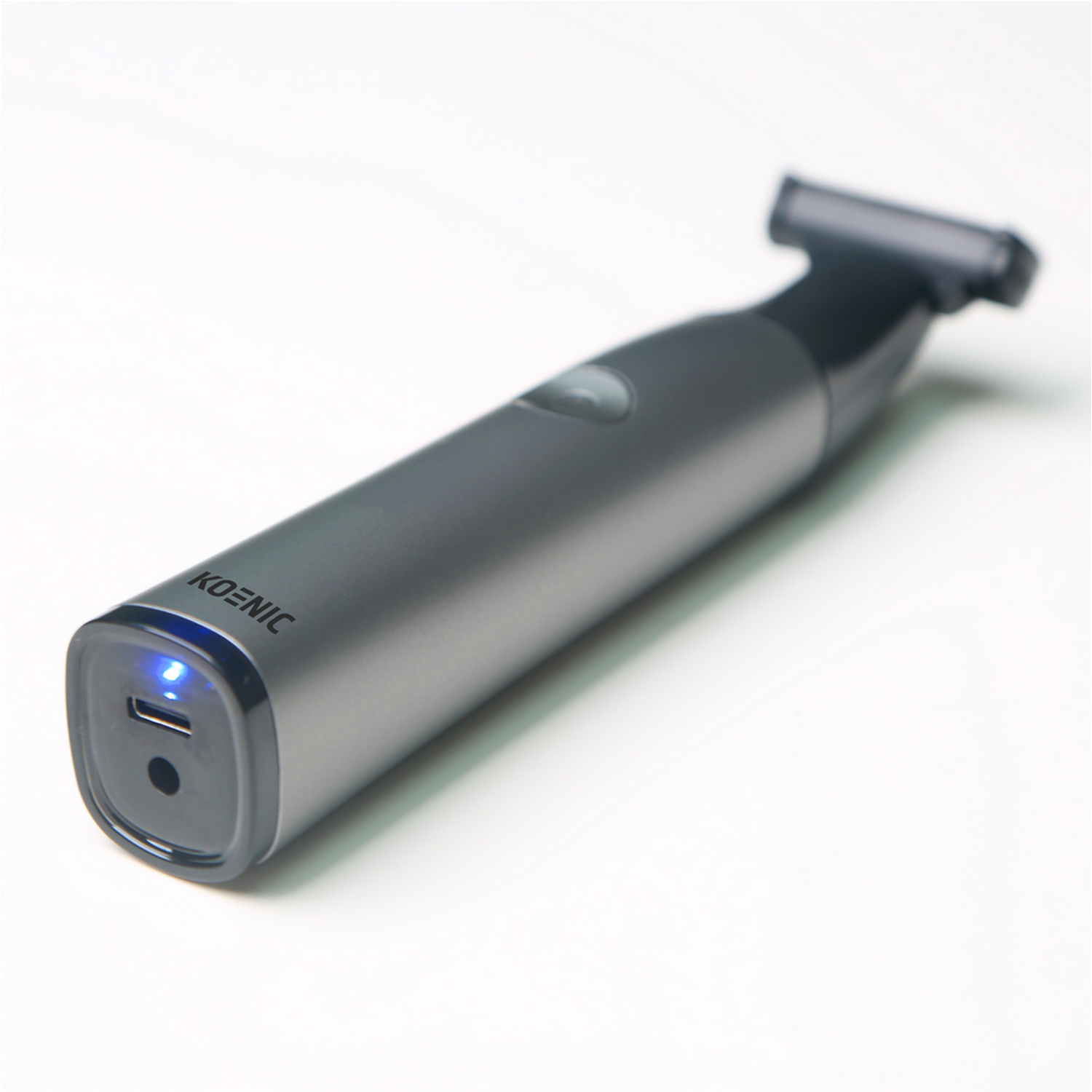 A gray Koenic electric razor with a black head, resting on a white surface.