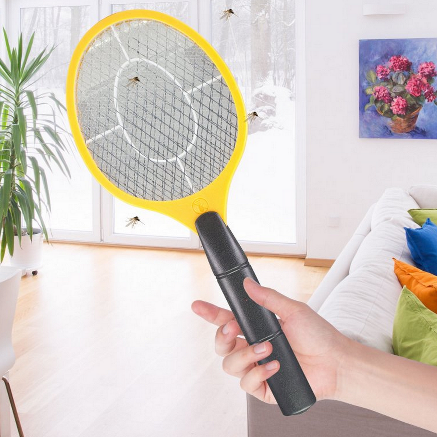 Een hand die een gele vliegenmepper vasthoudt, met insecten in de lucht.