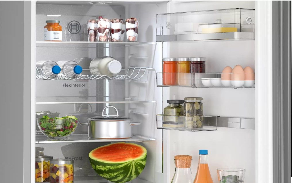 Refrigerador abierto con alimentos: sandía, ensaladas, frascos, botellas, huevos y más. Brillante y limpio.