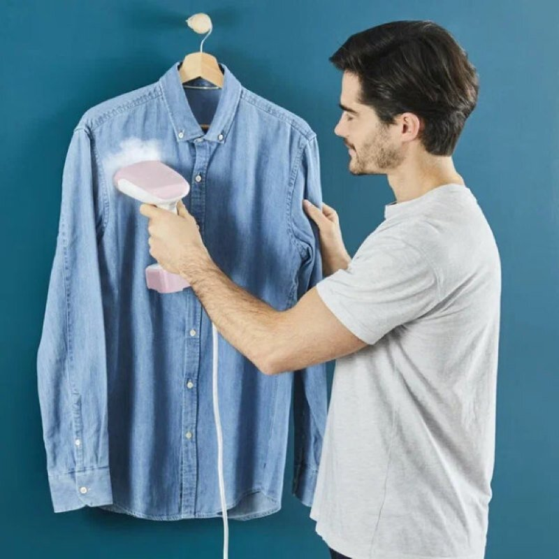Mężczyzna prasuje dżinsową koszulę. Trzyma różową parownicę, a koszula wisi na niebieskiej ścianie.