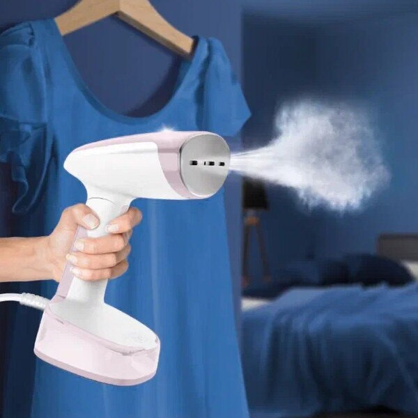 Ręczny parownik do ubrań parujący niebieską sukienkę. Biały i różowy parownik.