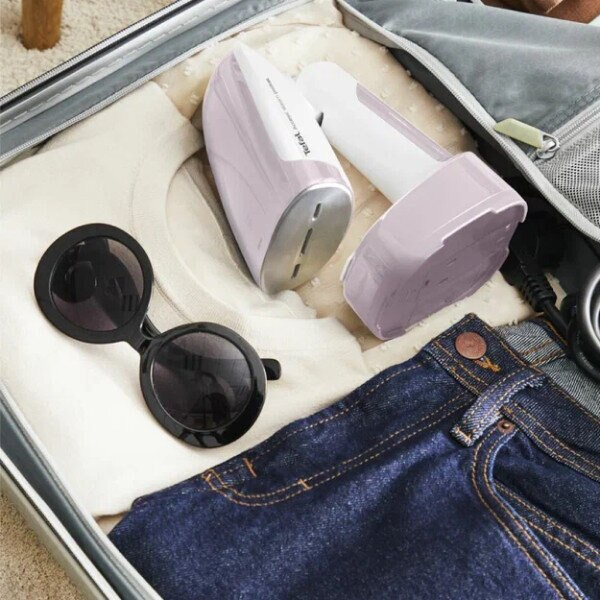 Otwarta walizka, zawierająca białą koszulę, okulary przeciwsłoneczne i dwa parownice podróżne.