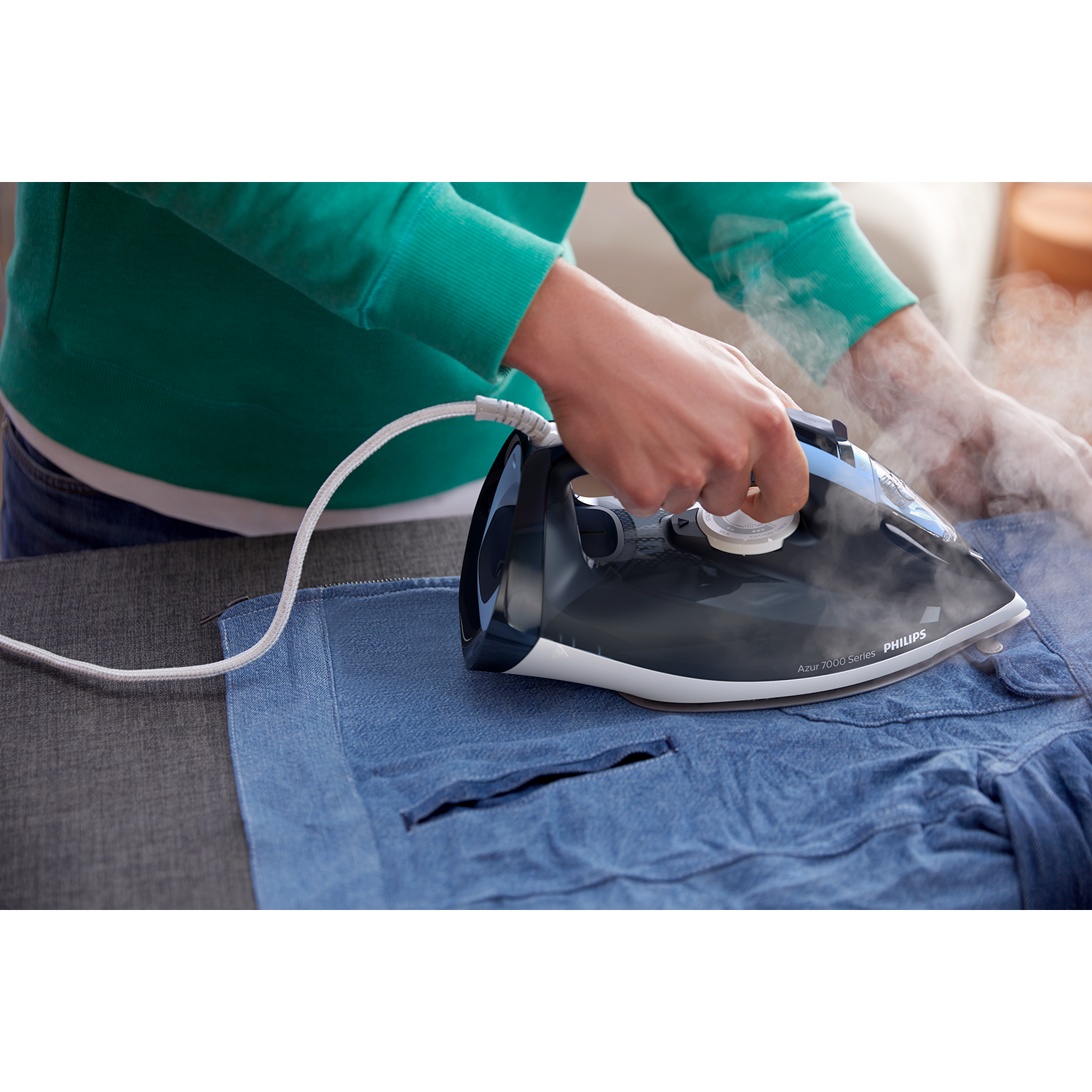 A person ironing blue denim. The iron is black and blue, steam is rising.