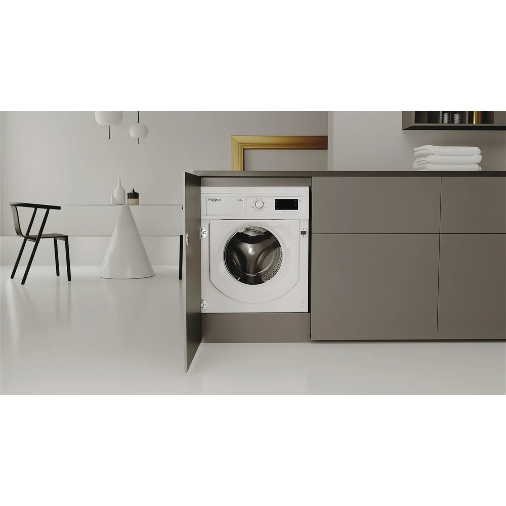 Egy fehér Whirlpool mosógép egy szürke szekrénybe szerelve, nyitott ajtóval.