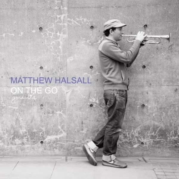 Albumcover: Matthew Halsall - On the Go. Mann spielt Trompete vor einer Betonmauer.