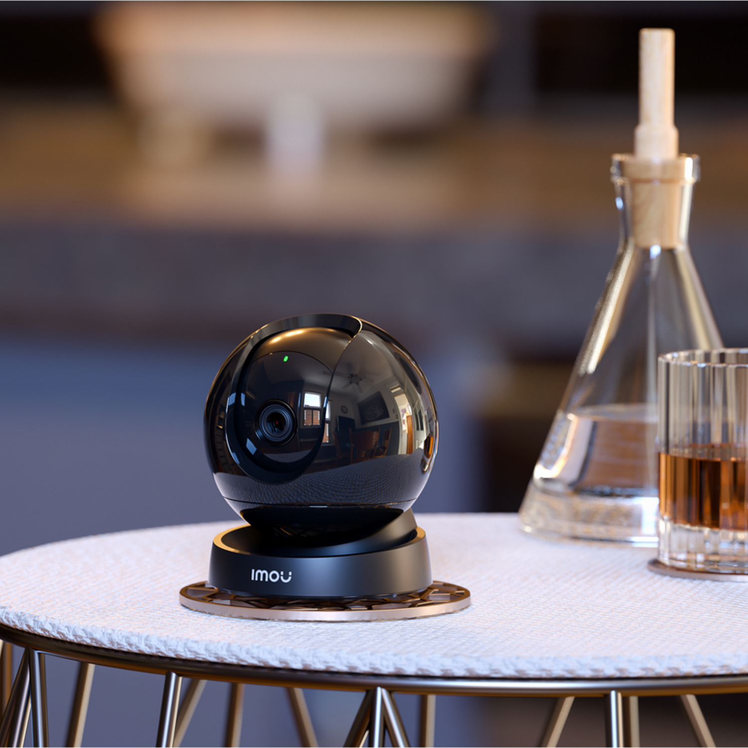 A black security camera on a table, with a glass of liquid and a bottle in the background.