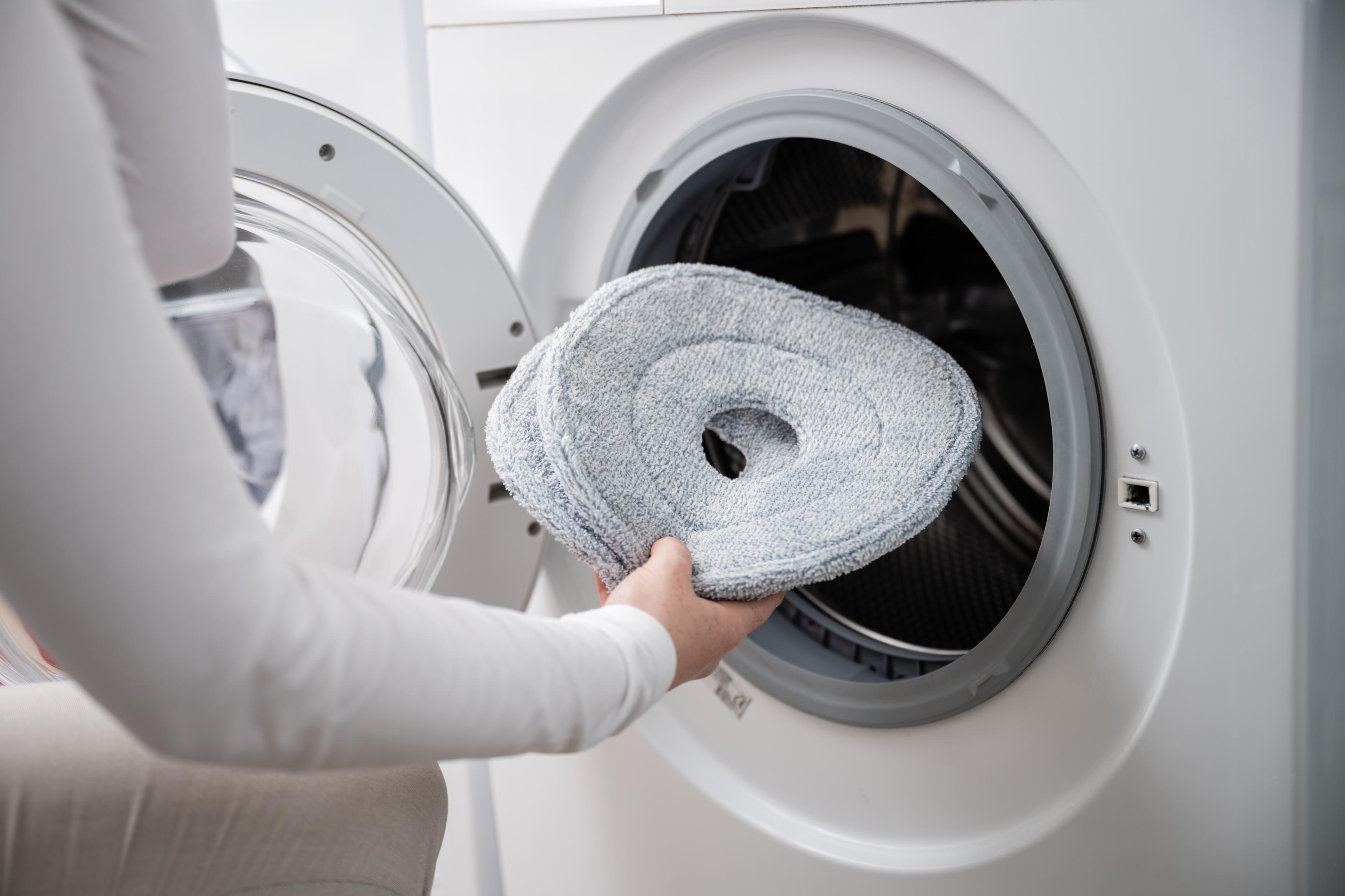 Eine Person legt einen Moppkopf in die Waschmaschine. Graue Moppköpfe.