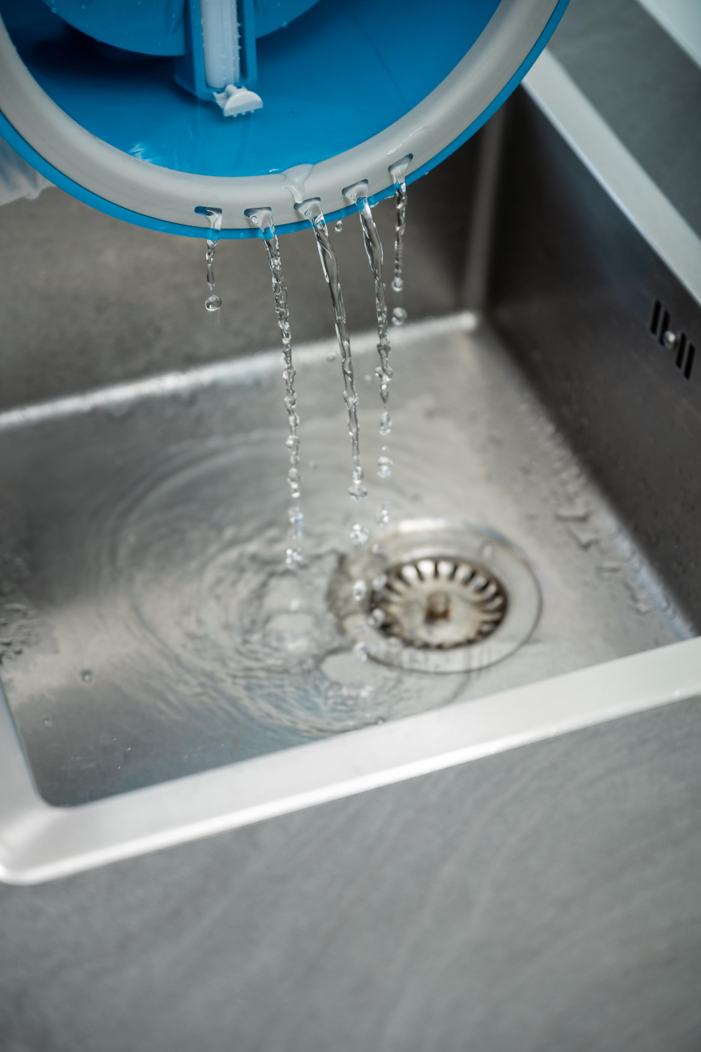 Wasser, das aus einem blau-weißen Objekt in ein Stahlbecken gießt, sichtbarer Abfluss.