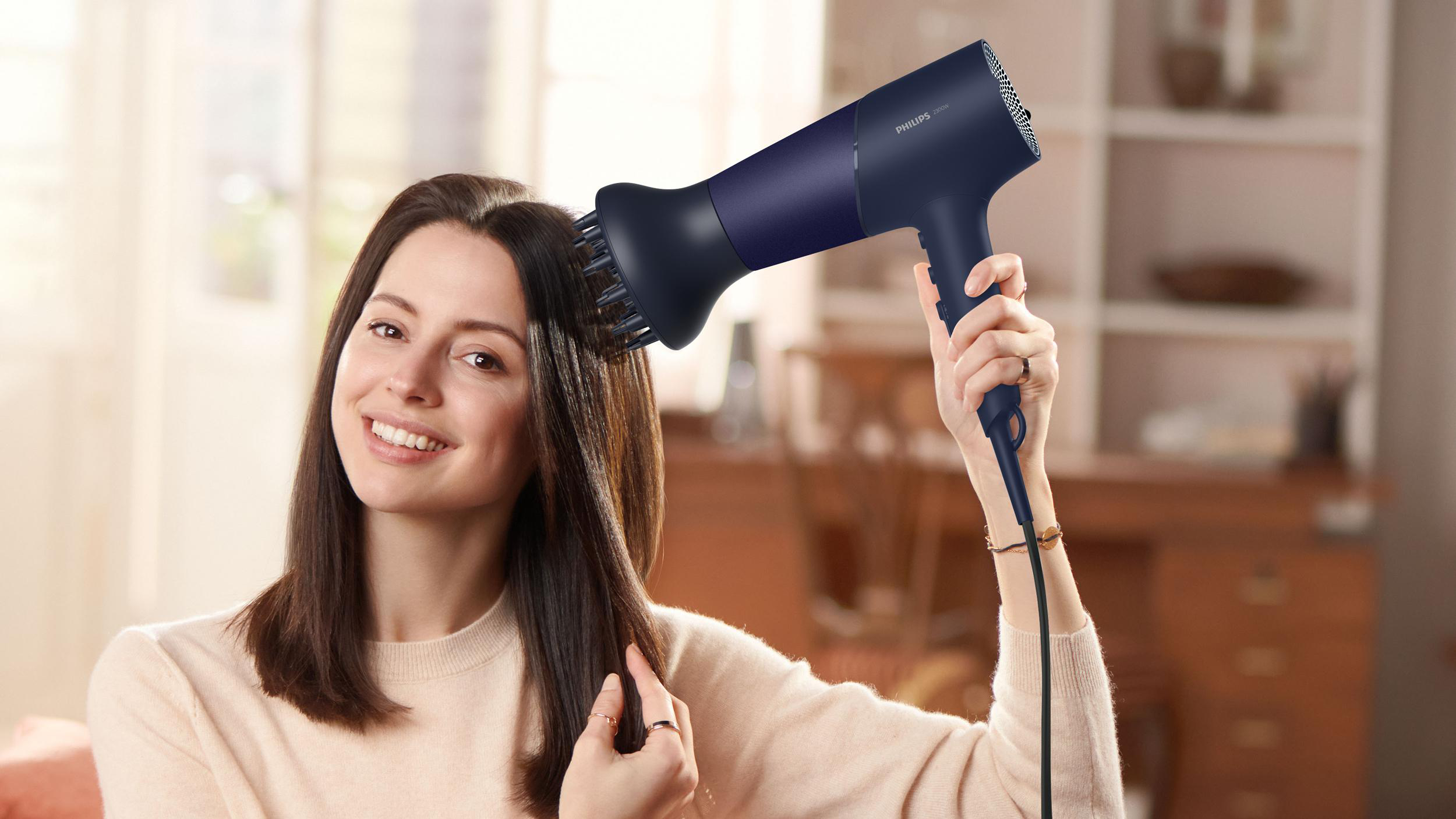 Eine Frau, die ihre Haare mit einem blau-schwarzen Philips Haartrockner trocknet.