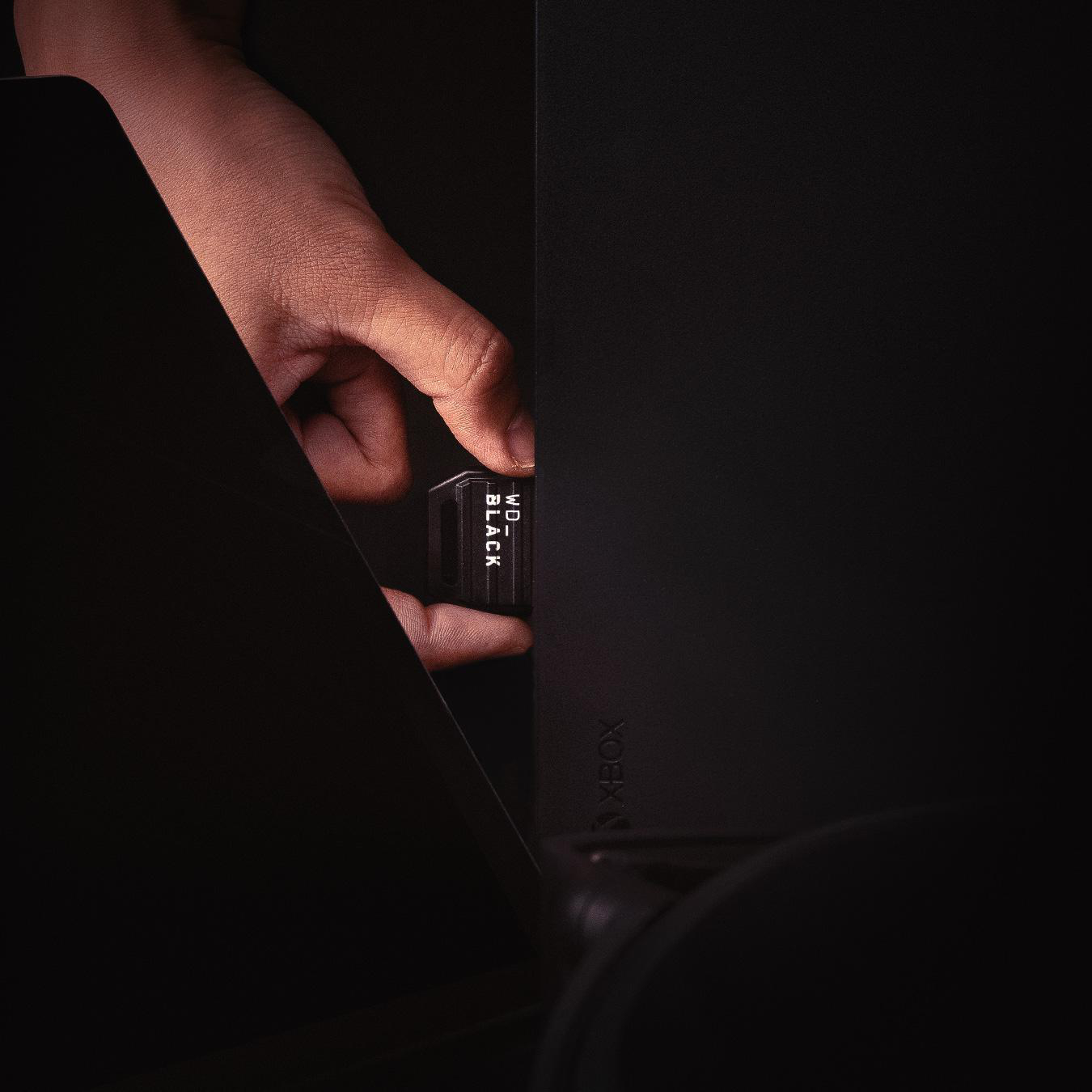 Eine Hand setzt eine schwarze WD_BLACK SSD in eine schwarze Xbox-Konsole ein.