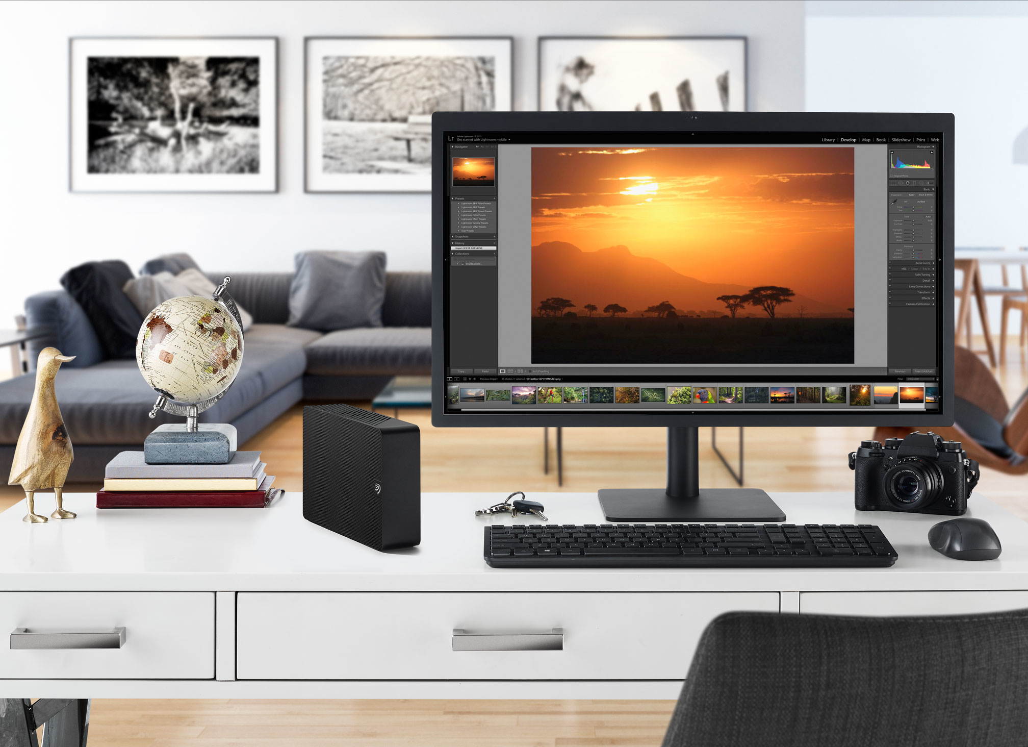 Schreibtisch mit Computer, Sonnenuntergangsfoto, Tastatur, Kamera, Globus und Dekorationen.