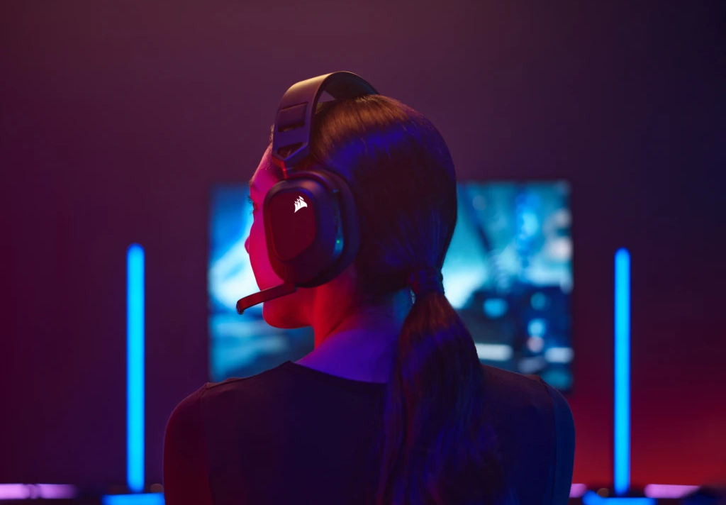 Fekete gamer fejhallgatót viselő személy, hátulról, piros és kék fényekkel megvilágított szobában.