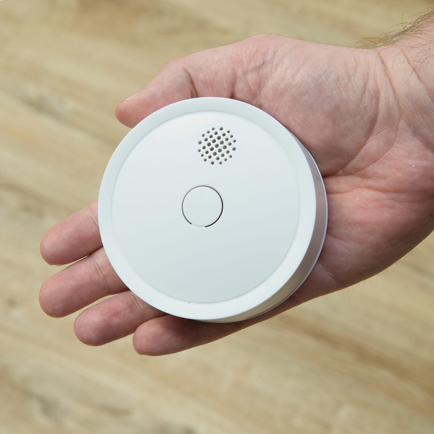 Witte rookmelder in de hand. De melder heeft een kleine luidspreker en een knop.