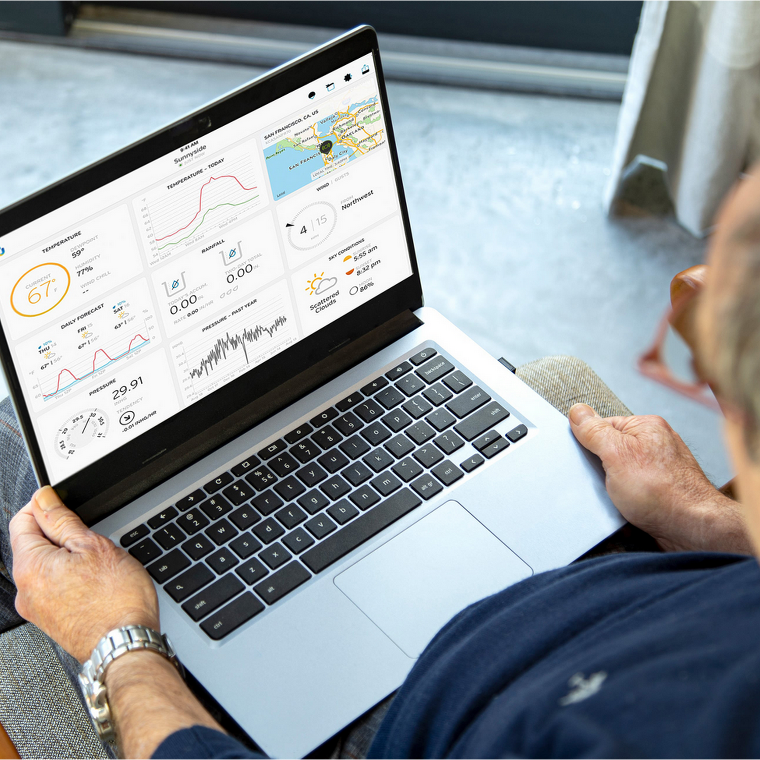 A person holding a laptop displaying weather data on the screen. The person is indoors.