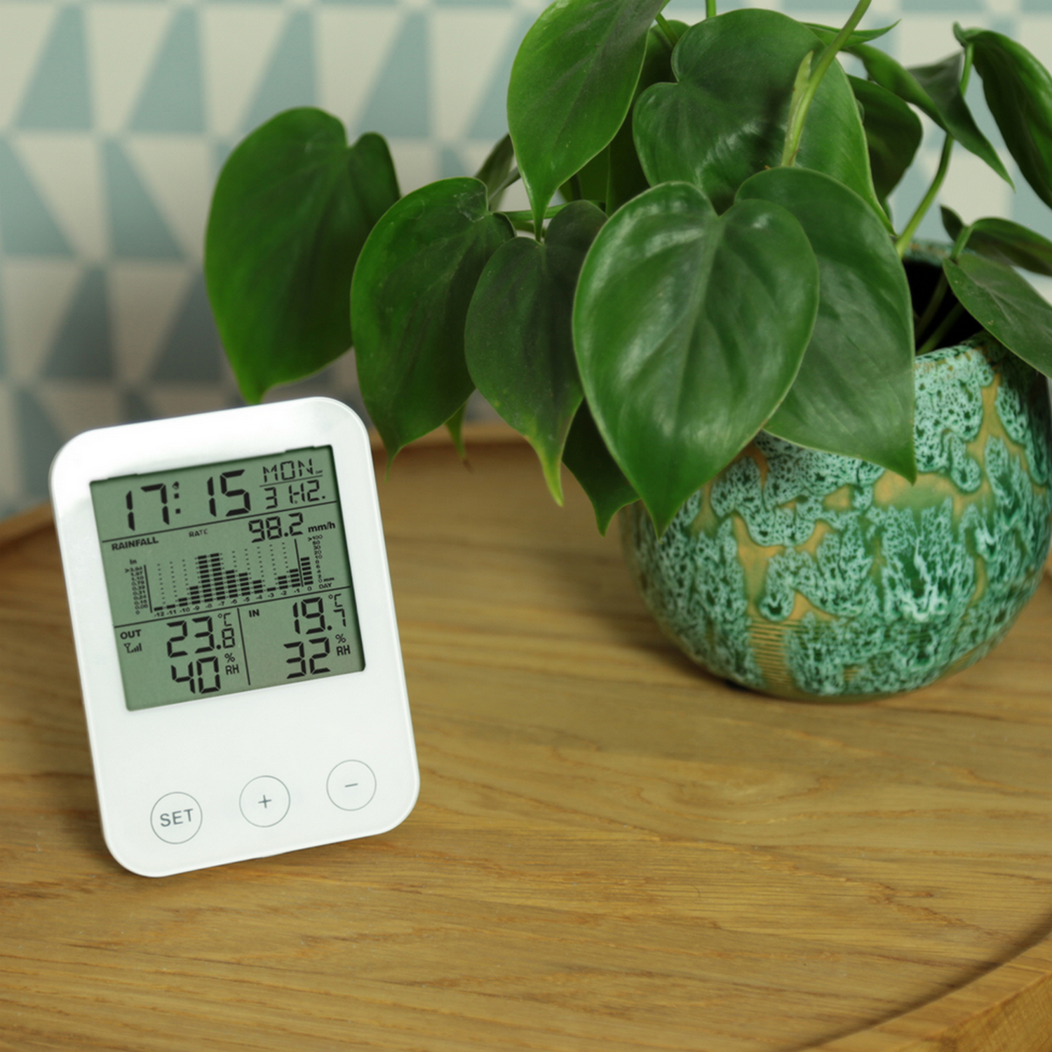 Digital display on a white device, plant, and wooden table.