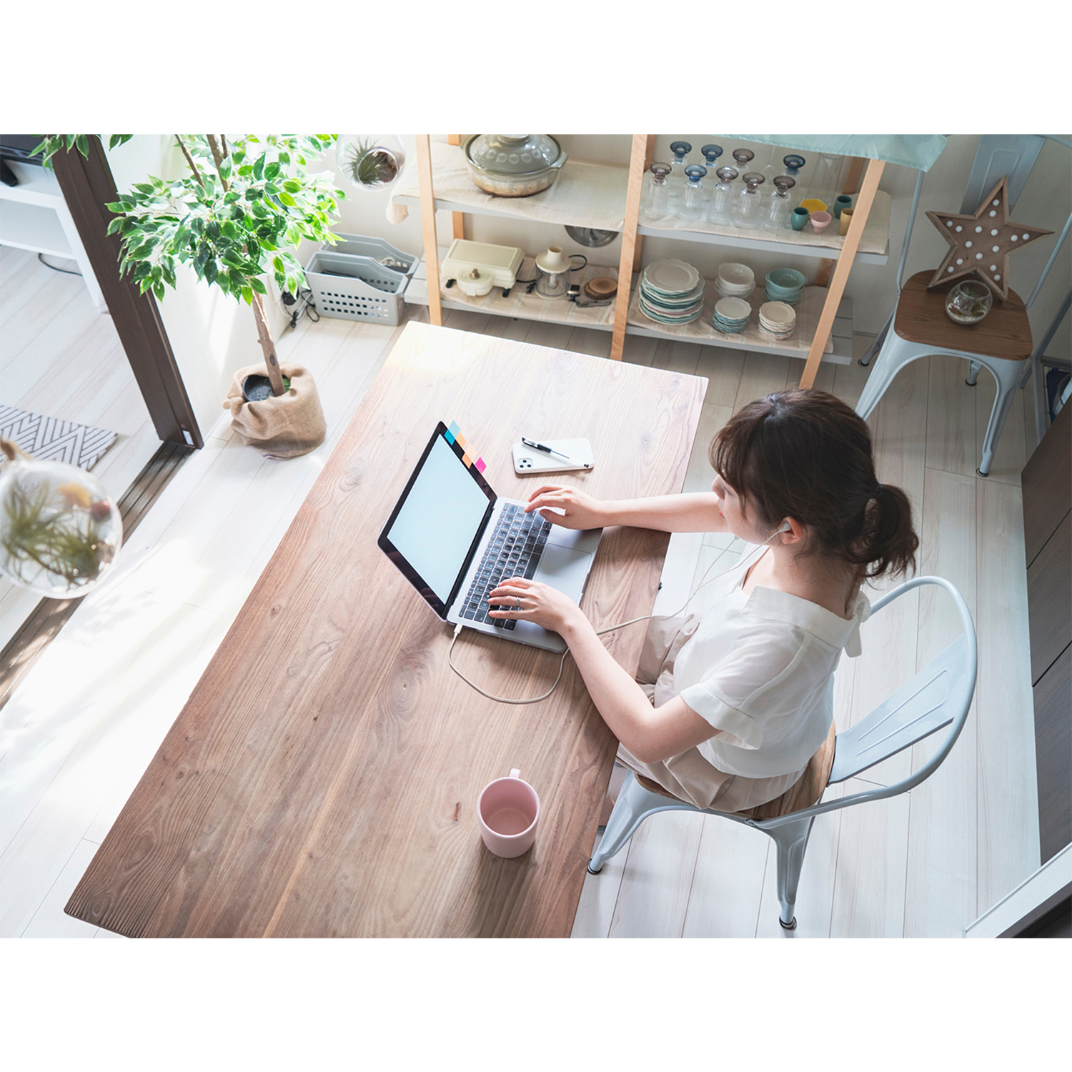 Donna che lavora su un laptop a un tavolo di legno, con una pianta e decorazioni.