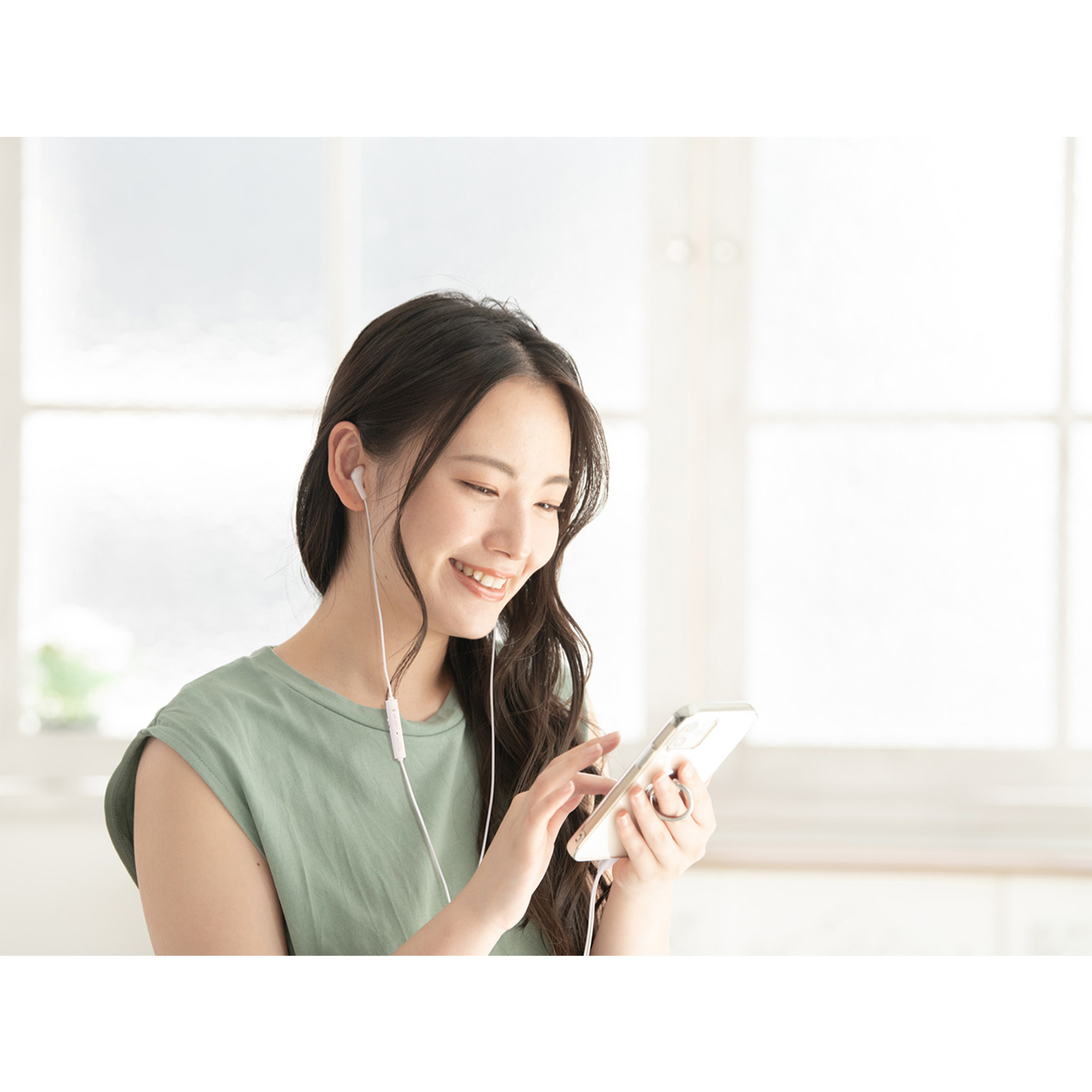 Una donna sorridente che usa uno smartphone con auricolari.