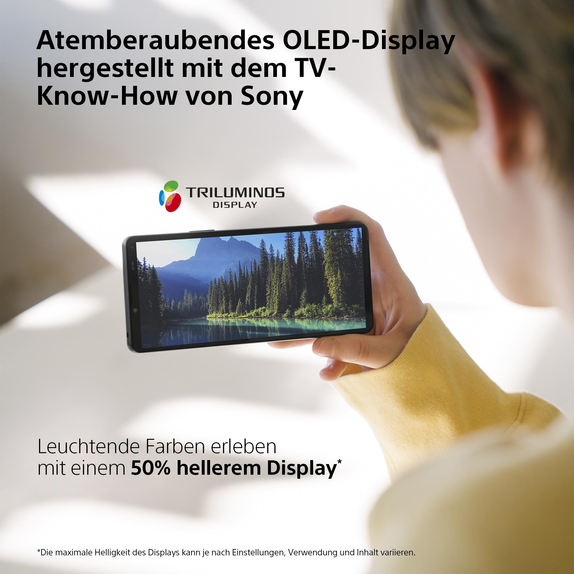 Person hält Telefon mit Waldszene, Text über OLED-Display.