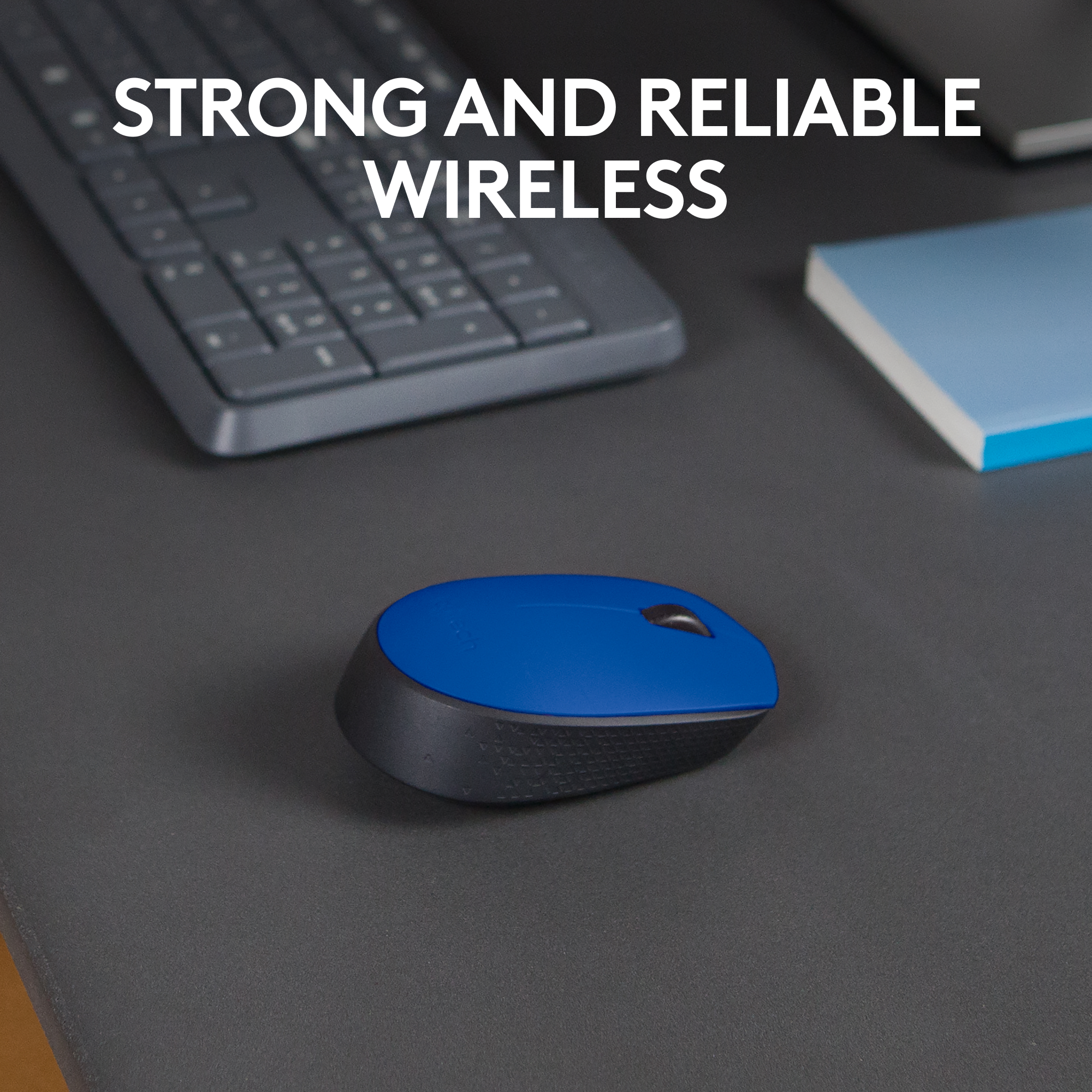 Une souris sans fil bleue et noire sur une surface grise. Clavier et bloc-notes sont également visibles.