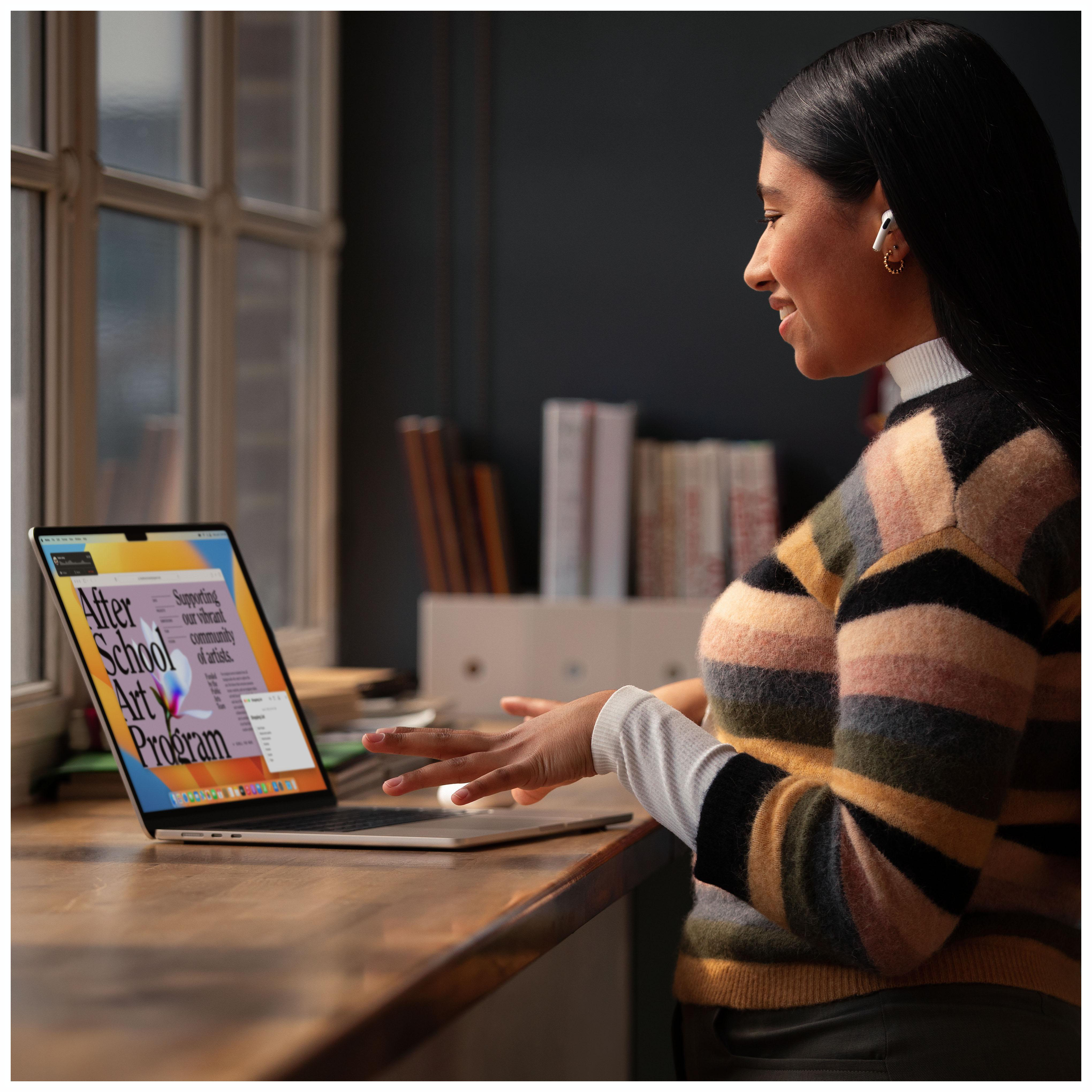 Frau benutzt Laptop, lächelt, in der Nähe eines Fensters. Laptop zeigt Text über ein Kunstprogramm.