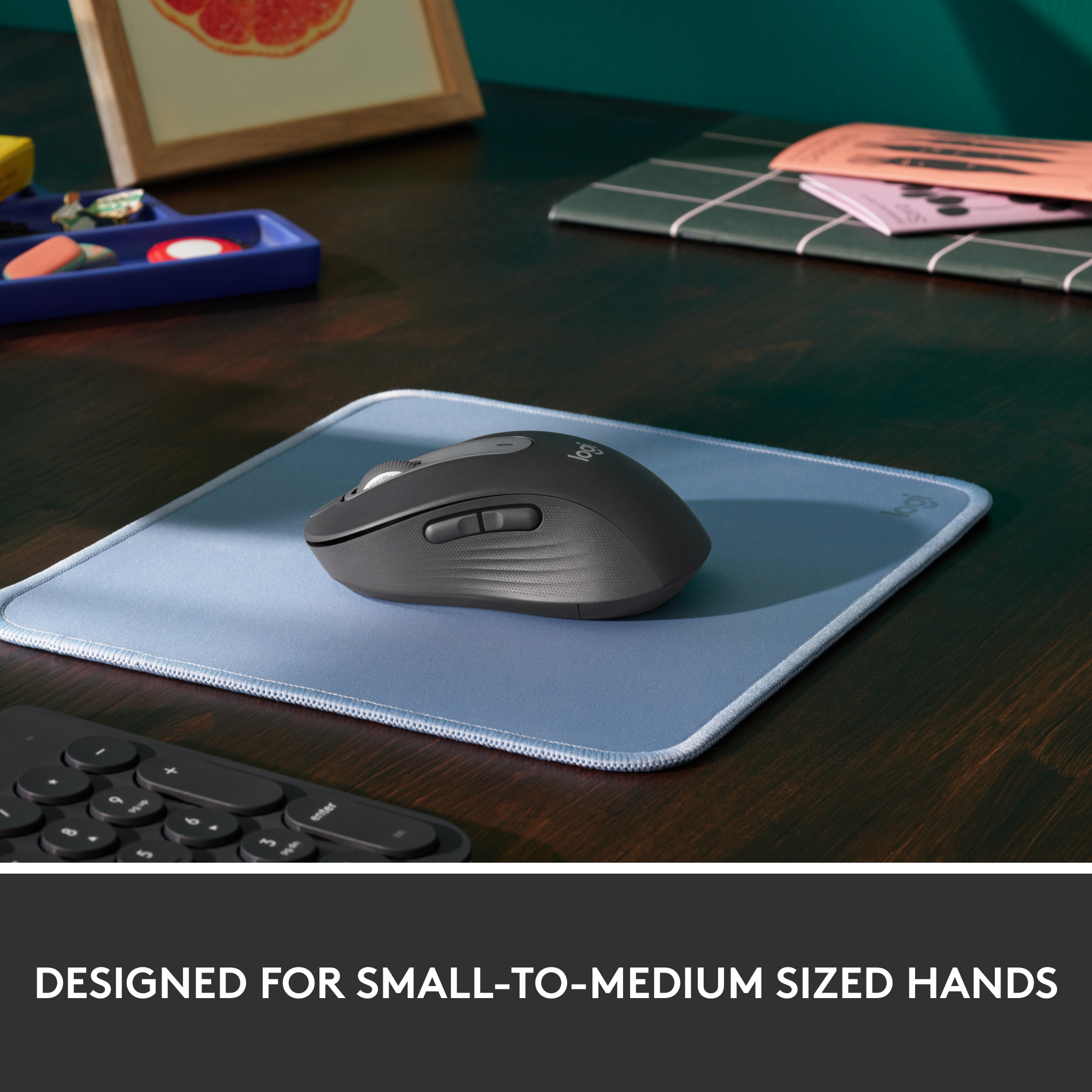Une souris noire sur un tapis de souris bleu. Il y a un clavier en arrière-plan. Conçu pour les mains petites à moyennes.