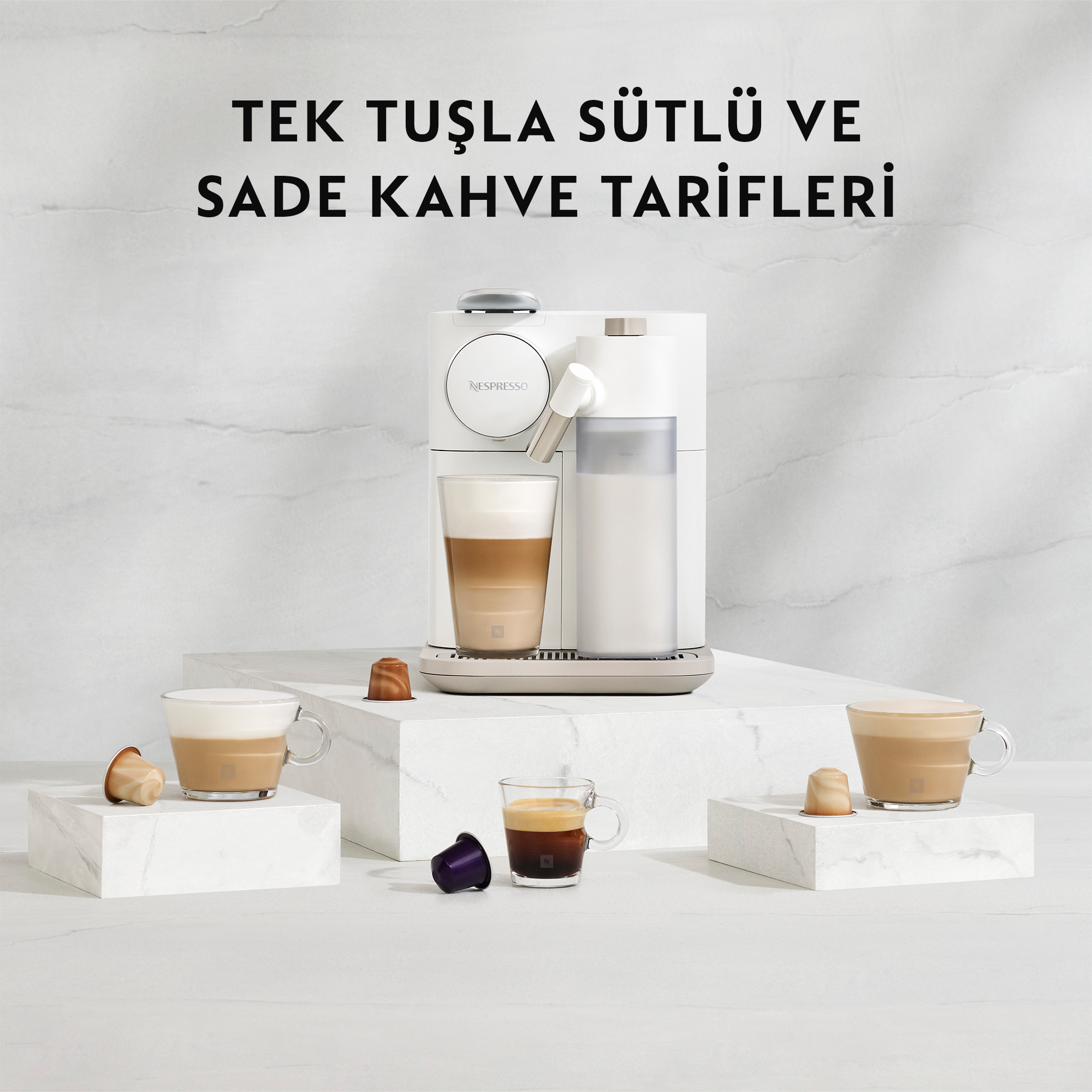 Beyaz bloklar üzerinde kahve kapsülleri ve fincanlarla beyaz bir kahve makinesi.
