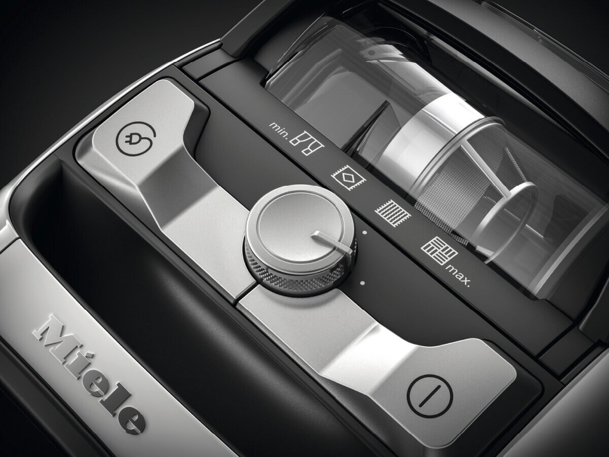 Elementy sterowania odkurzaczem: pokrętło, przyciski i przezroczysty pojemnik na kurz, w skali szarości.