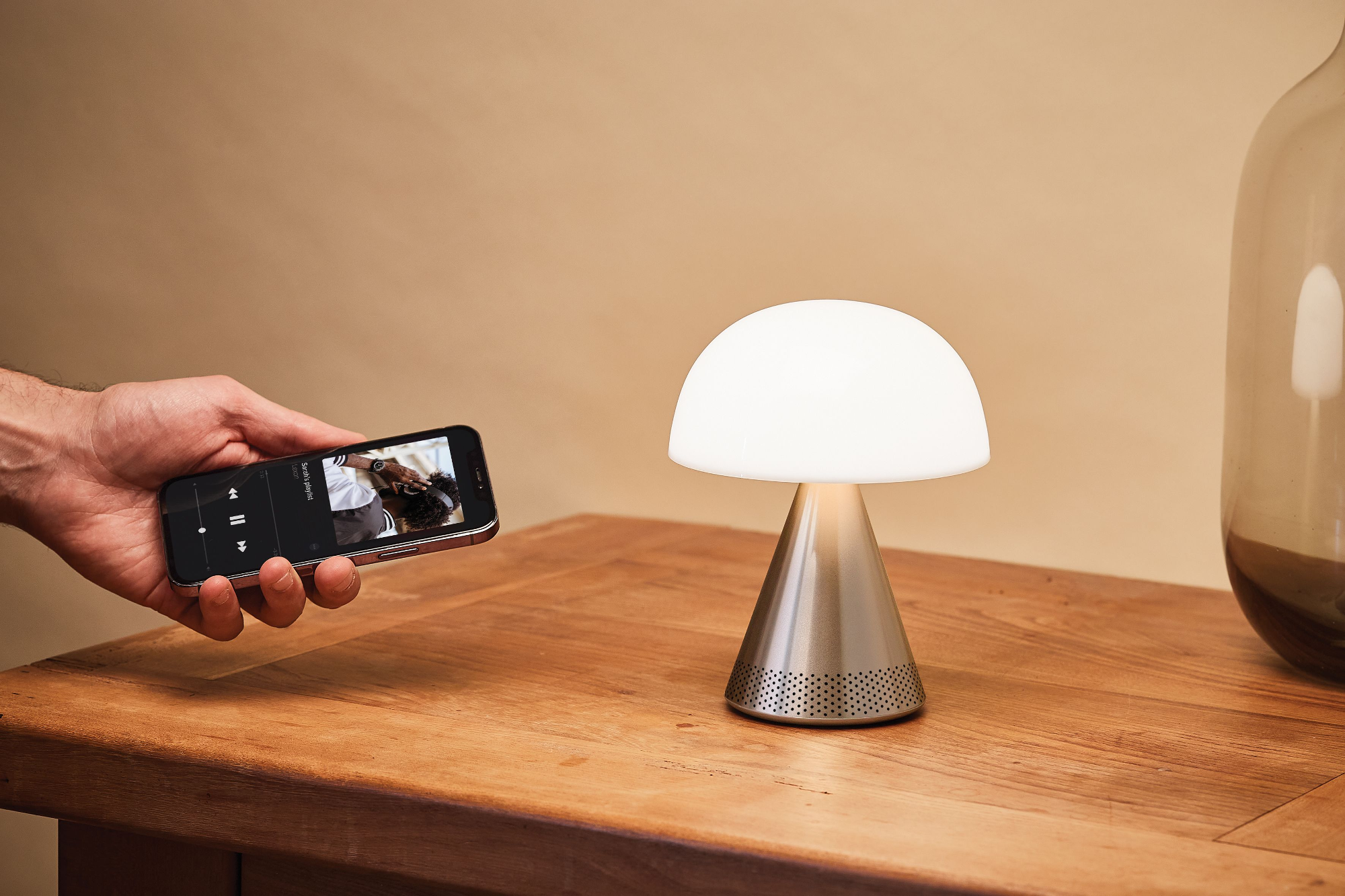 Une personne tient un téléphone jouant de la musique à côté d'une lampe en forme de champignon sur une table.