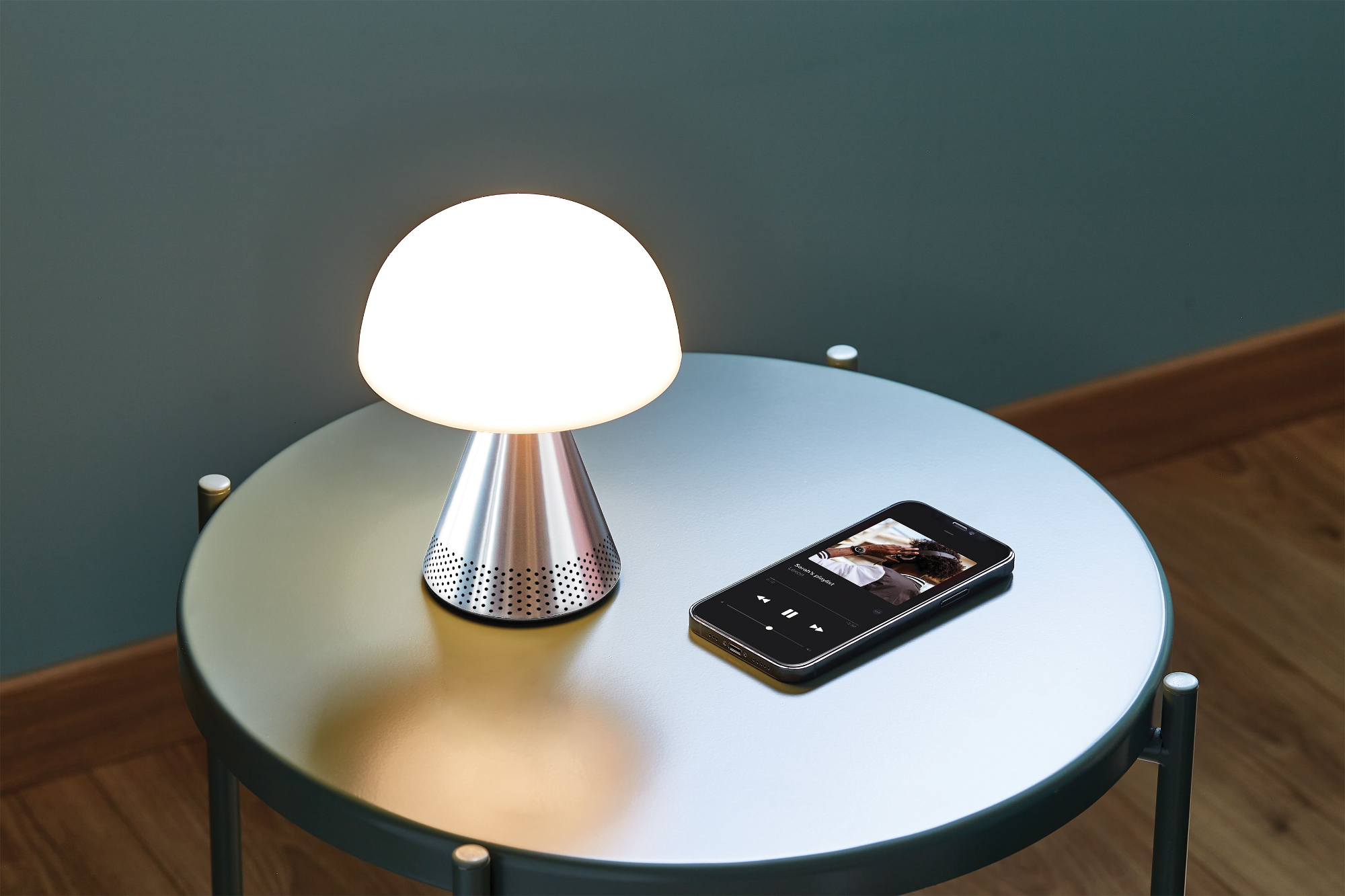 Une lampe en forme de champignon et un smartphone sur une table. Le téléphone affiche une interface musicale.