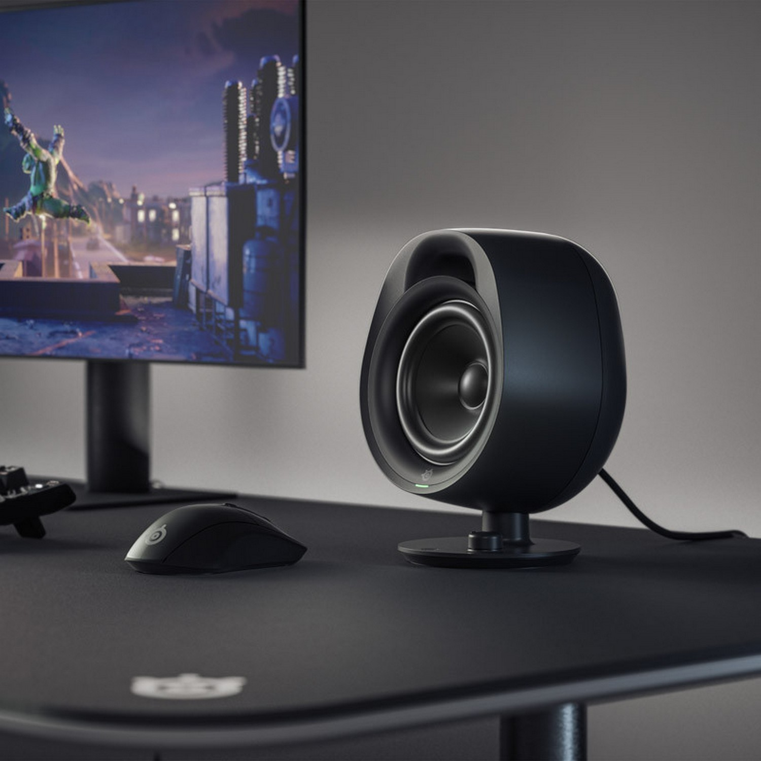A black speaker next to a computer monitor and a mouse. The speaker is on a black desk.