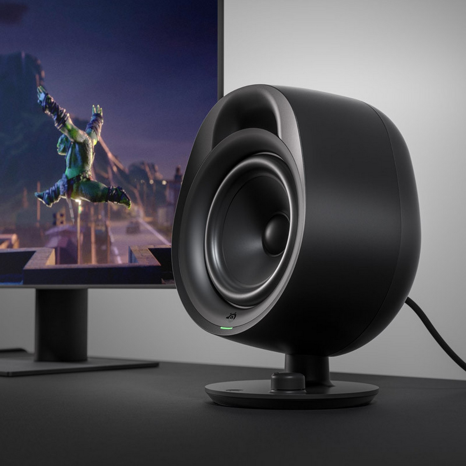 A black speaker with a green light, near a computer monitor.
