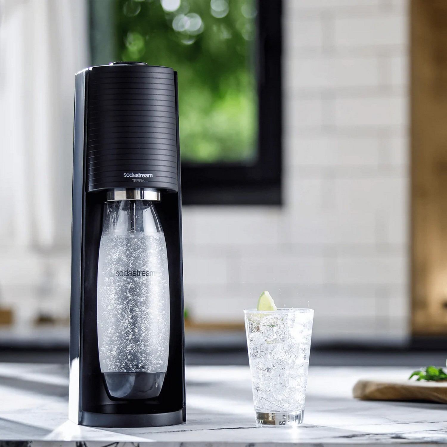 Une machine SodaStream noire avec une bouteille et un verre d'eau gazeuse avec une tranche de citron vert.
